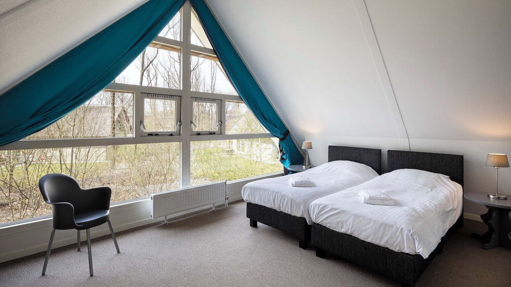 Un dormitorio con dos camas, una silla y un ventanal con cortinas.