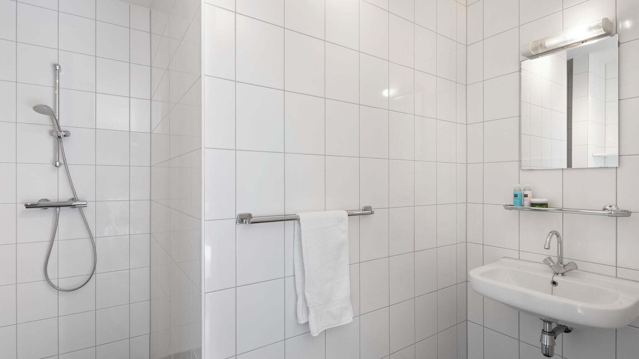 A modern bathroom with white tiles, a shower, a sink, and a towel rack.