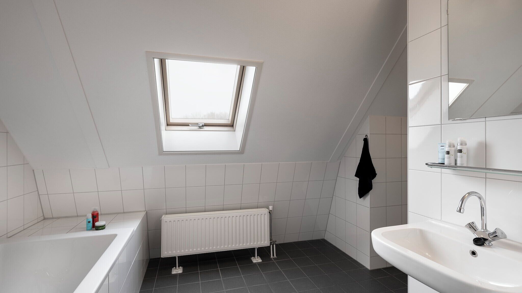 A modern bathroom with a skylight, a bathtub, a sink, and a radiator.