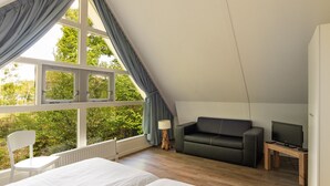 A bedroom with a bed, a sofa, a TV, and a window with curtains. - Summio Buitenplaats de Marke van Ruinen (Ruinen)