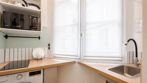 A compact kitchen with a washing machine, a microwave, and a window with blinds. - Stylish Duplex in Vibrant Central Paris (Paris)
