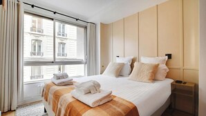A hotel room with a large bed, a window with curtains, and a view of buildings outside. - SERENE AMBIANCE,JUST MOMENTS FROM TROCADÉRO – CHAMPS ELYSEES AT RUE DE L'AMIRAL (Paris)