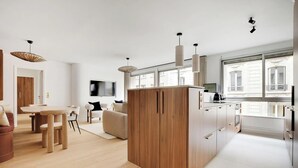 A modern kitchen with wooden cabinets, a dining area with a table and chairs, and a living room with a sofa and TV. - SERENE AMBIANCE,JUST MOMENTS FROM TROCADÉRO – CHAMPS ELYSEES AT RUE DE L'AMIRAL (Paris)