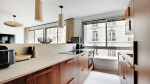 A modern kitchen with wooden cabinets, a large window, and pendant lighting. - SERENE AMBIANCE,JUST MOMENTS FROM TROCADÉRO – CHAMPS ELYSEES AT RUE DE L'AMIRAL (Paris)