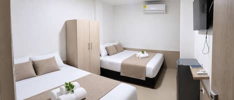 A hotel room with two beds, a wardrobe, a television, and a desk with a computer.