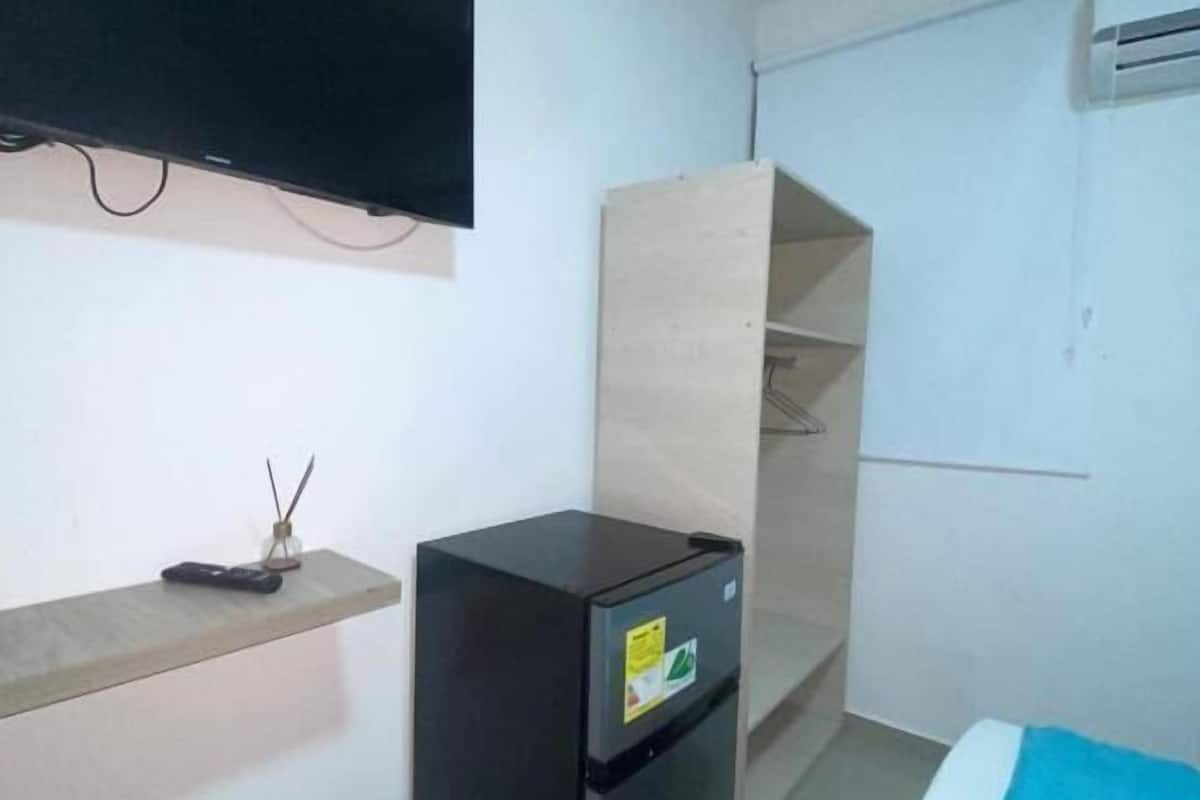 A small, clean room with a bed, a TV mounted on the wall, a small refrigerator, and a wooden wardrobe.