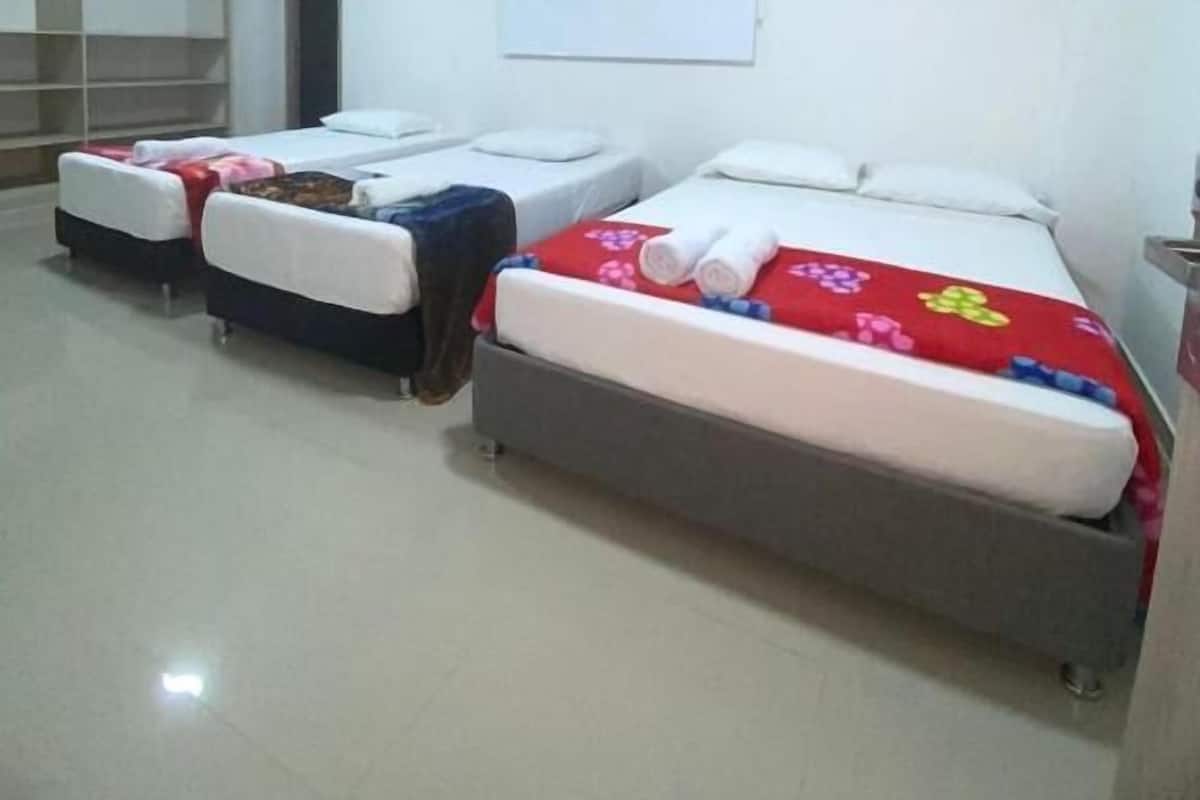 A hotel room with three single beds, a whiteboard on the wall, and a small table with a lamp.