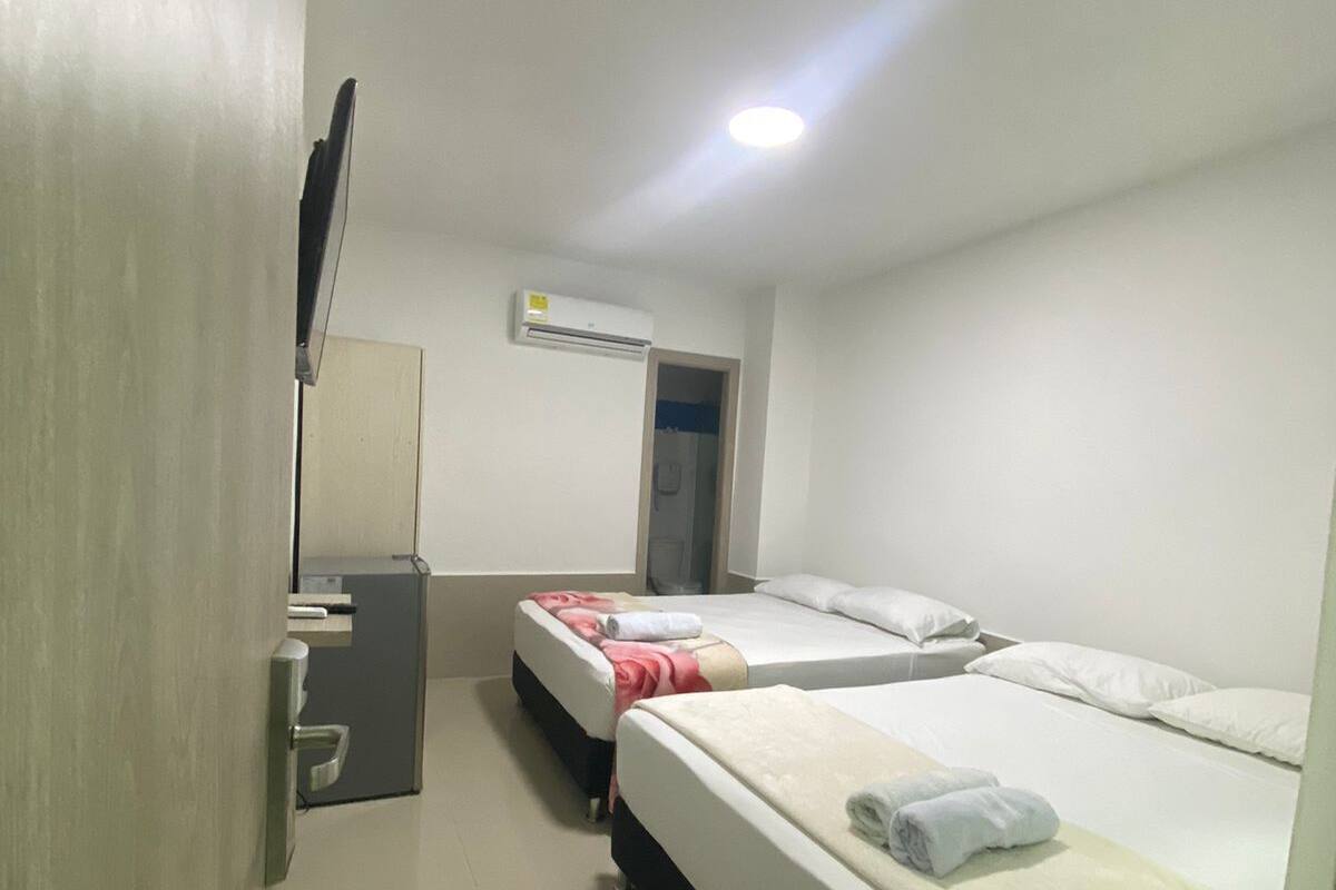 A hotel room with two beds, a small desk, a television, and an air conditioning unit.