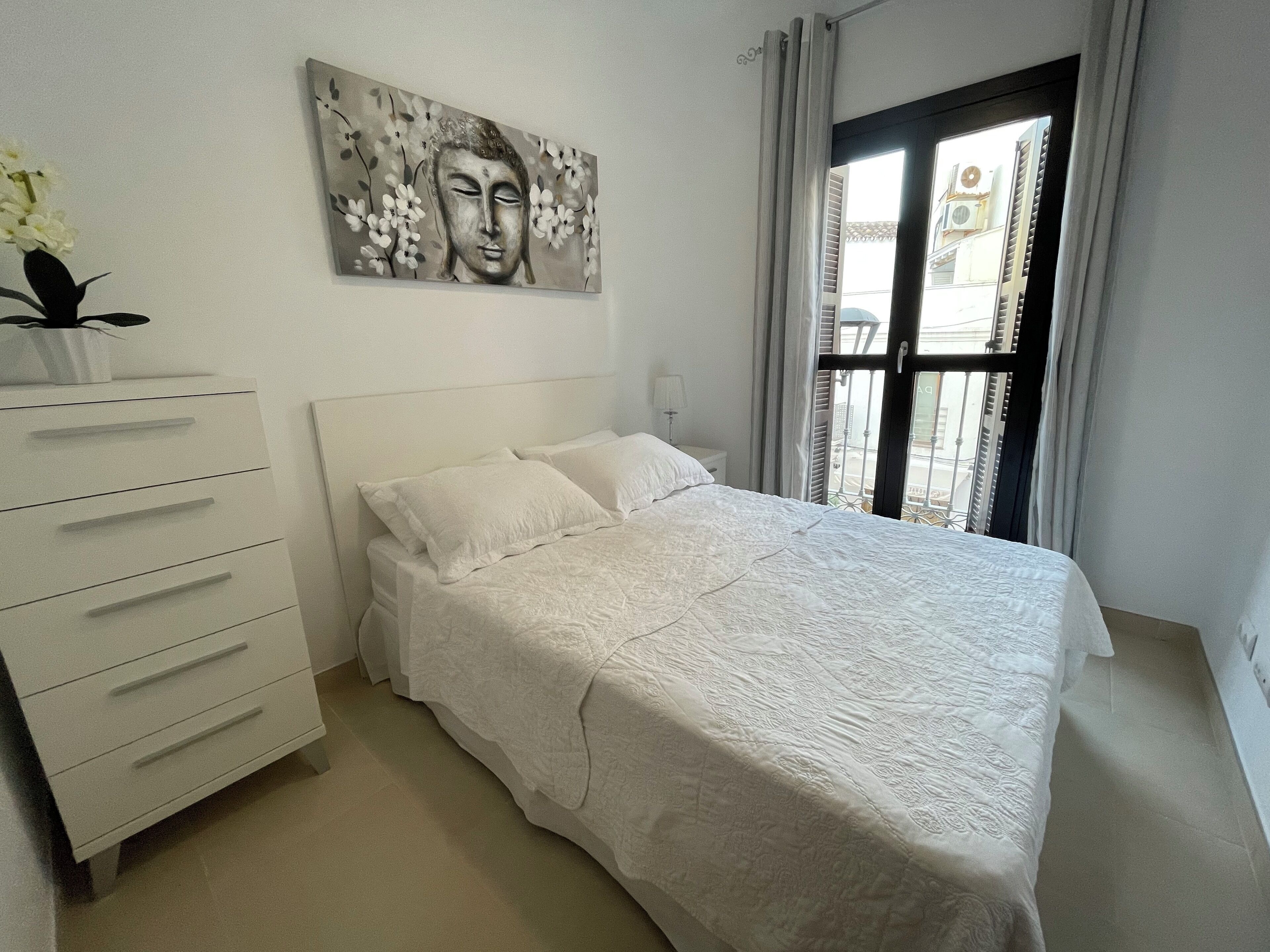 A bedroom with a bed, a dresser, a painting, and a window with curtains.