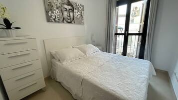 Un dormitorio con cama, cómoda, un cuadro y ventana con cortinas.
