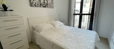 A bedroom with a bed, a dresser, a painting, and a window with curtains.