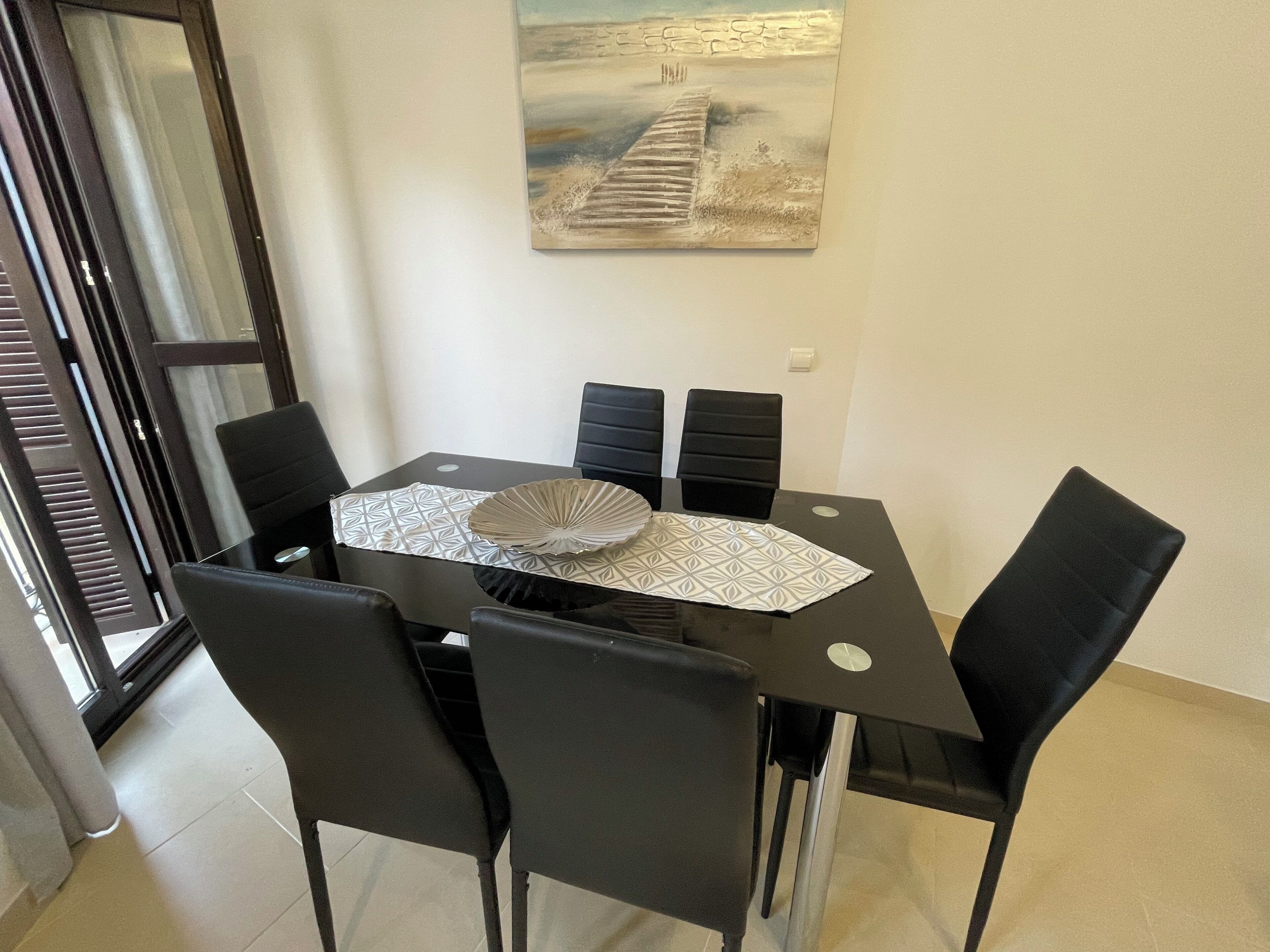 Uma sala de jantar com mesa, cadeiras e um quadro na parede.