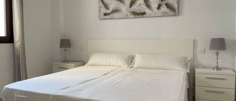 A neatly made bed with white linens, two bedside tables with lamps, and a wall-mounted artwork.