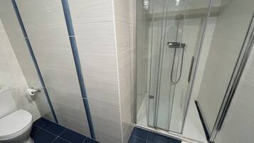 Un baño con ducha de vidrio, inodoro y piso de azulejos azules.