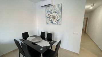 Una zona de menjador amb taula i cadires negres, una paret blanca amb un quadre floral i una unitat de aire condicionat.