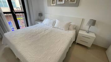 A neatly made bed with a white duvet, a bedside table with a lamp, and a wall with decorative metal art pieces.