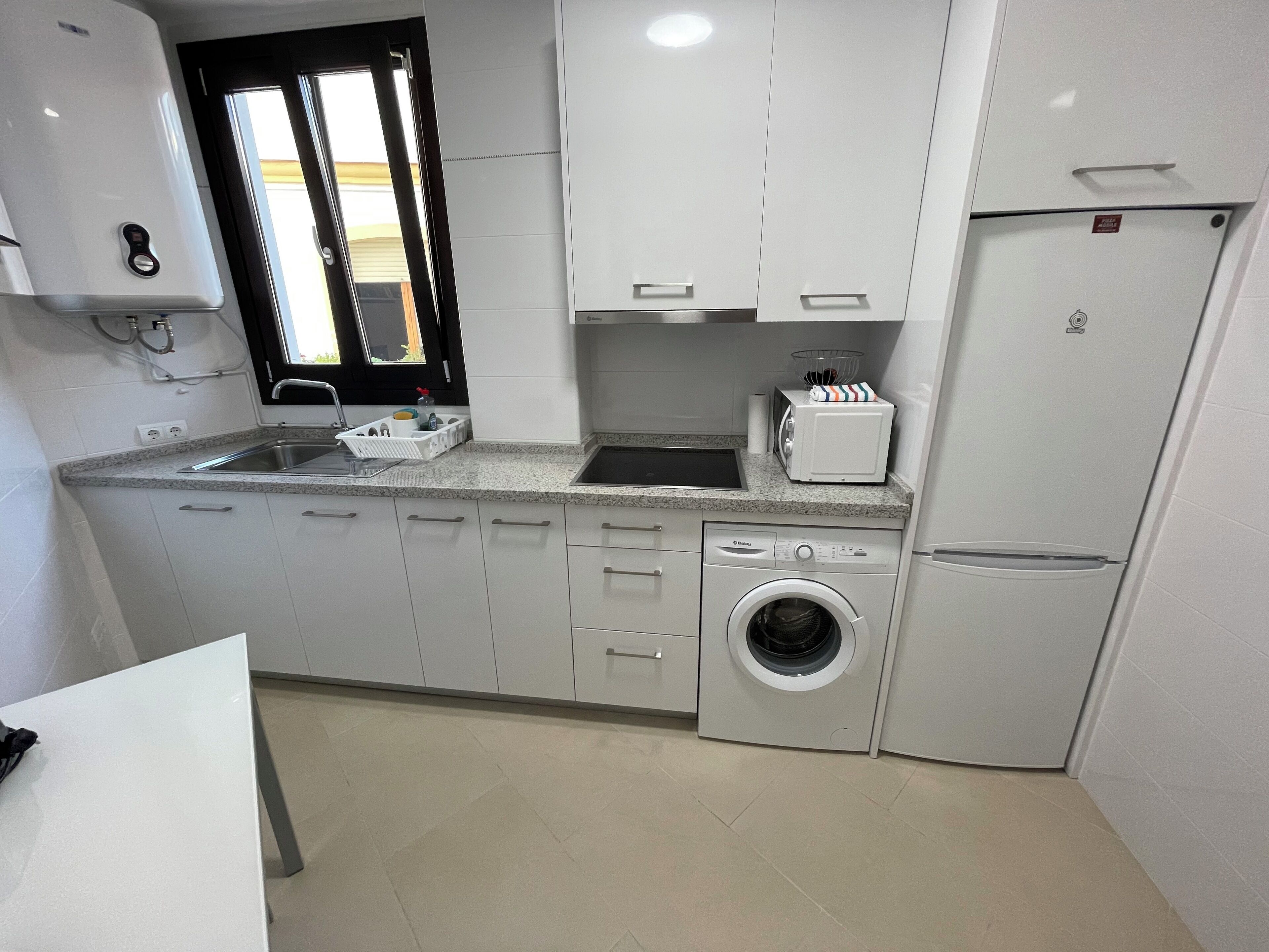 Cocina compacta con lavadora, microondas y lavabo.