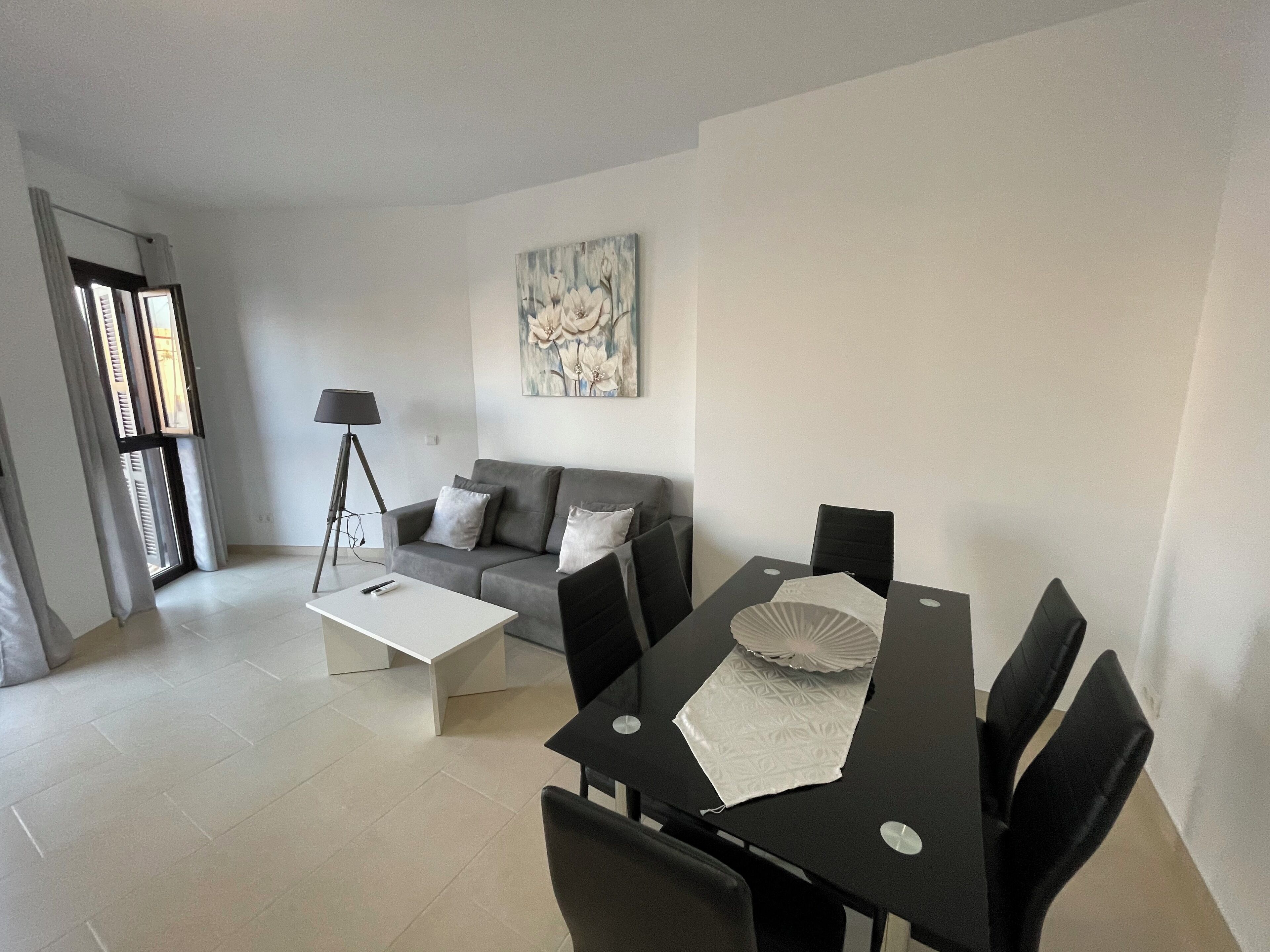 A modern living room with a grey sofa, a white coffee table, a dining table with chairs, and a floor lamp.