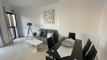 A modern living room with a grey sofa, a white coffee table, a dining table with chairs, and a floor lamp.