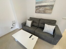 Una sala de estar moderna con un sofá gris, dos almohadones estampados, una mesa de centro blanca, un control remoto y una regleta de enchufes.
