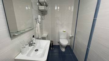 Un baño compacto con un lavabo blanco, un inodoro y un estante de vidrio sobre el lavabo.