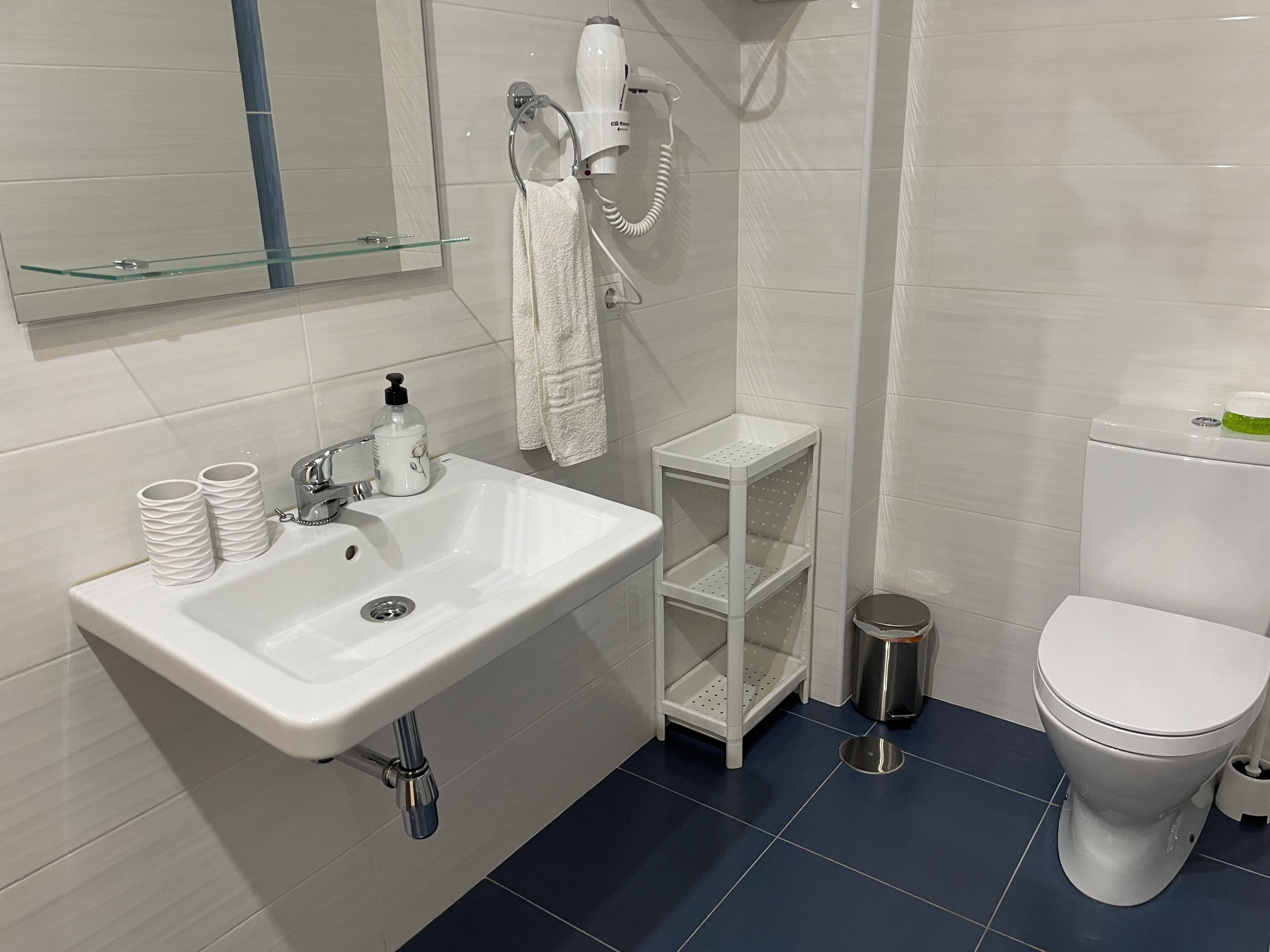 Un baño moderno con lavamanos blanco, secador de pelo, inodoro y cubo de basura.