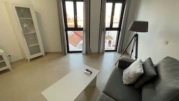 Una sala de estar moderna con un sofá gris, una mesa de centro blanca, una lámpara de pie y un aparador de vidrio.
