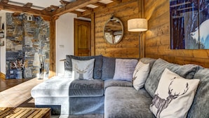 A cozy living room with a stone wall, wooden beams, a large sofa, and a mirror. - Cosy 74m2 View Garden | SkiLift 250m | Parking Bus (Chamonix-Mont-Blanc)