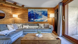 A cozy living room with a sectional sofa, a wooden coffee table, and a large mountain painting on the wall. - Cosy 74m2 View Garden | SkiLift 250m | Parking Bus (Chamonix-Mont-Blanc)