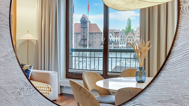A modern hotel room with a large window, a dining table, and a sofa. - Lion Apartments - Apartment in Old Town (Gdansk)