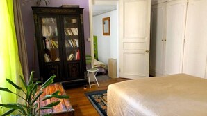 A bedroom with a bed, a wooden cabinet, a chair, and a radiator. - L'appartement Boulnois (Paris)