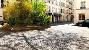 A cobblestone street with buildings on either side, a tree with yellow leaves, and a scooter parked on the sidewalk. - L'appartement Boulnois (Paris)