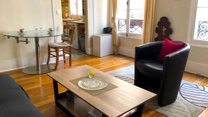 A living room with a glass table, a black leather sofa with a red pillow, and a wooden coffee table. - L'appartement Boulnois (Paris)
