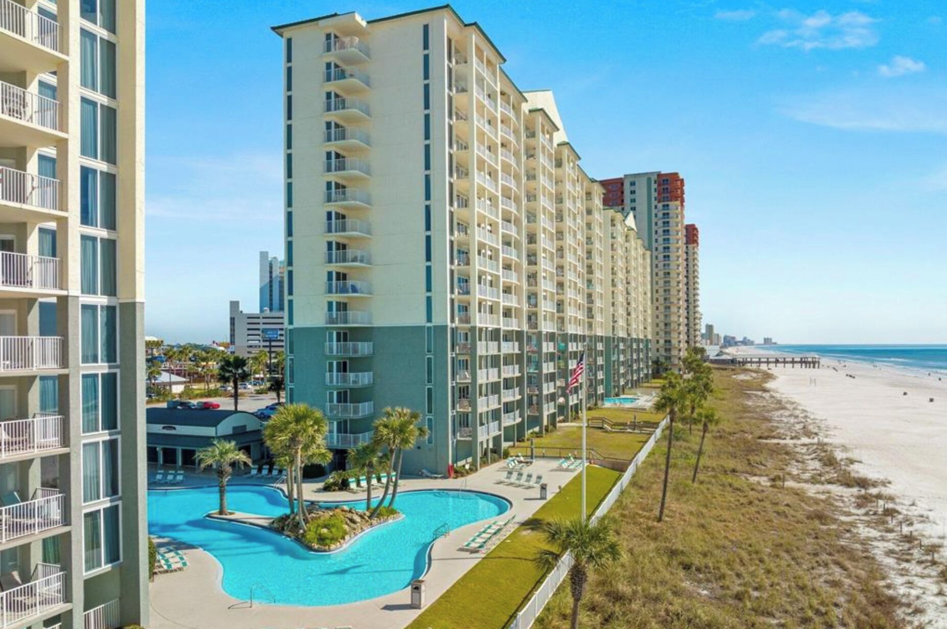 A high-rise hotel with multiple balconies, a swimming pool, and a beach view.