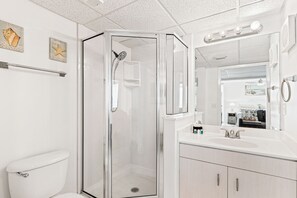 Un baño moderno con ducha de vidrio, inodoro blanco, tocador con lavamanos y espejo.