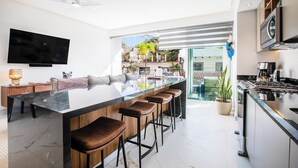 Une cuisine moderne dotée d’un grand îlot central, de tabourets de bar, d’un téléviseur à écran plat et d’un ventilateur de plafond.