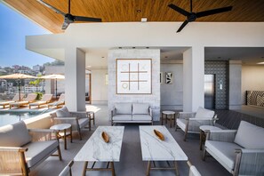 Un área de lounge moderna al aire libre con asientos, piscina y vistas de la ciudad.