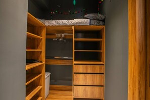Un dressing accessible sans porte, avec des étagères en bois, une tringle à vêtements et un lit avec des oreillers.