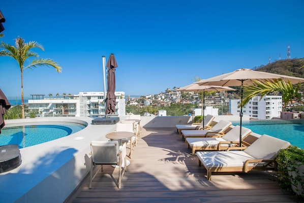 Un espace piscine aménagé sur le toit, avec des chaises longues, une table et des parasols.