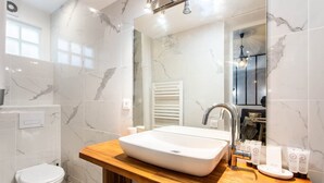 A modern bathroom with a marble backsplash, a wooden vanity, a white sink, a mirror, and toiletries.