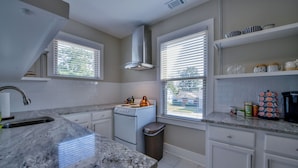 Una cocina moderna con gabinetes blancos, encimera de granito, extractor de acero inoxidable y una ventana con persianas.
