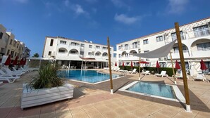 A pool area with multiple pools, lounge chairs, and umbrellas. - Amore Protaras Apartments (Paralimni)