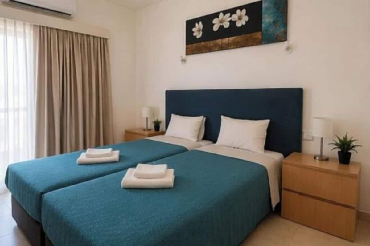A hotel room with two beds, a nightstand with a lamp, and a painting on the wall.