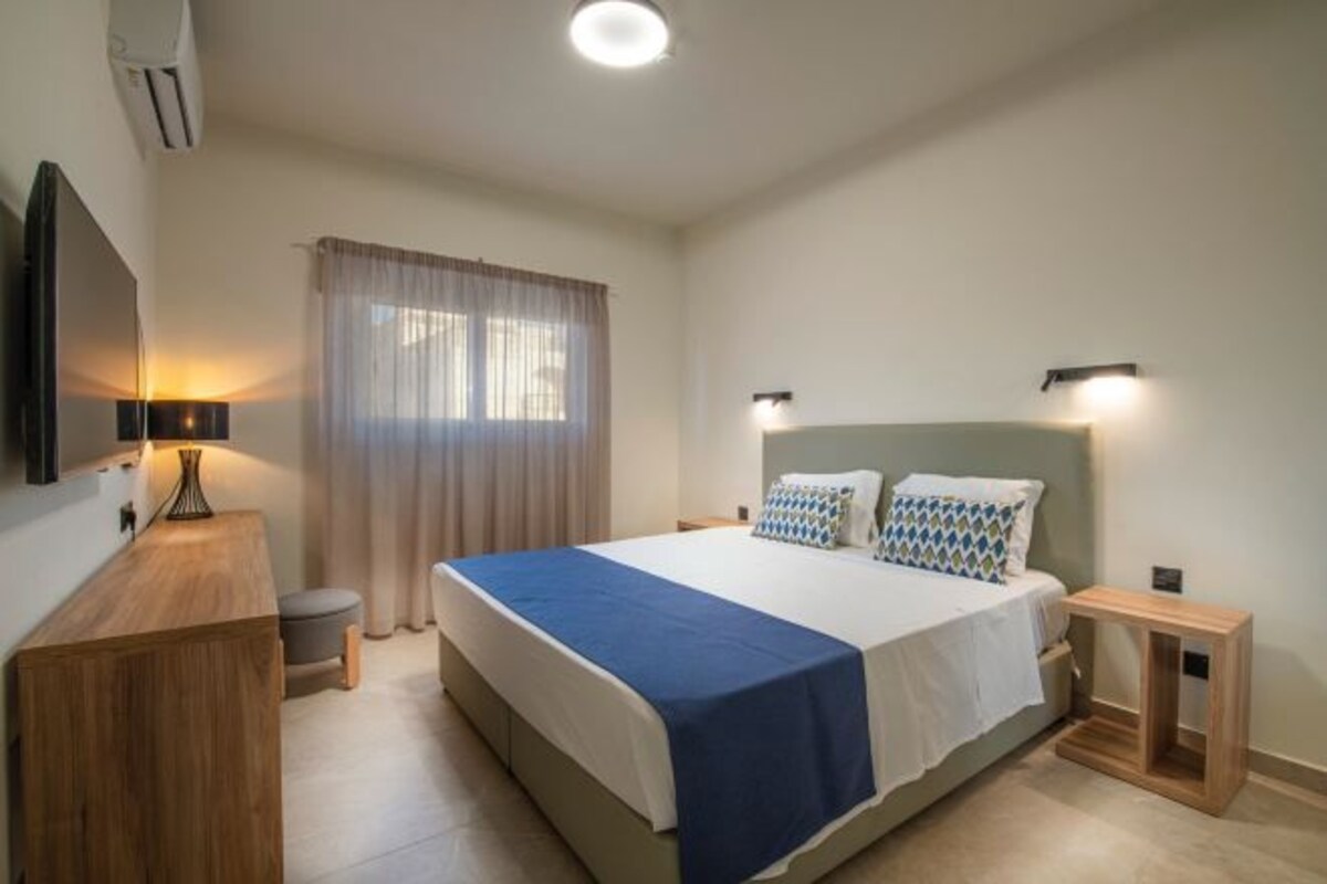 A modern bedroom with a large bed, bedside tables, a desk, and a flat-screen TV.