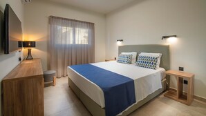 A modern hotel room with a large bed, bedside tables, a desk, and a TV mounted on the wall. - Amore Protaras Apartments (Paralimni)