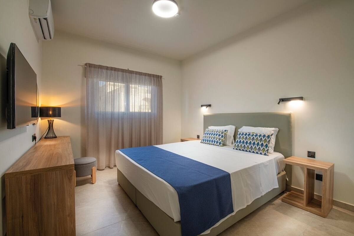A modern hotel room with a large bed, bedside tables, a desk, and a TV mounted on the wall.