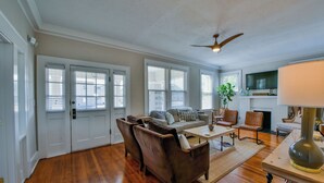 Un salon spacieux doté d’un parquet, d’un canapé gris, de fauteuils en cuir marron, d’une table basse et d’un ventilateur de plafond.