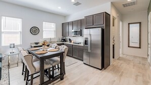 Una cocina moderna con armarios oscuros, electrodomésticos de acero inoxidable y un comedor con mesa y sillas de madera.