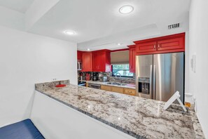 A modern kitchen with red cabinets, stainless steel appliances, and a marble countertop. - NPR (Naples)