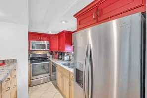 A modern kitchen with red cabinets, stainless steel appliances, and a built-in oven.